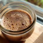 Overhead close-up of creamy chocolate overnight oats in a glass jar, showing the foamy top layer.