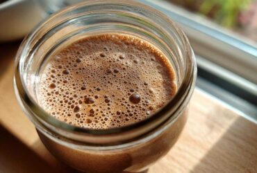 Overhead close-up of creamy chocolate overnight oats in a glass jar, showing the foamy top layer.