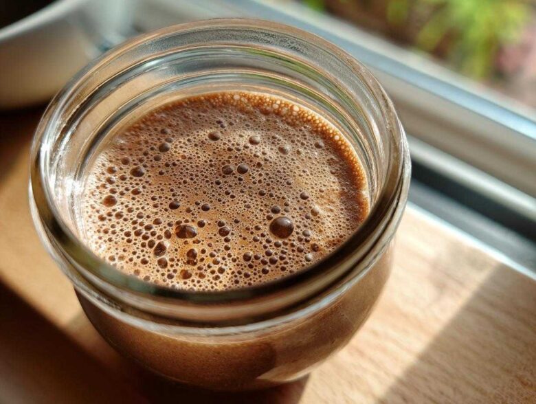 Overhead close-up of creamy chocolate overnight oats in a glass jar, showing the foamy top layer.