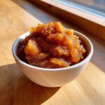 A close-up of chunky, spiced applesauce sprinkled with cinnamon served in a small white bowl.