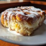 A close-up, sunlit serving of fluffy Cinnamon roll casserole topped with thick white icing.