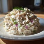 A mound of creamy cottage cheese chicken salad mixed with celery and red onion, garnished with fresh dill on a white plate.