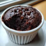 Close-up of a rich, dark chocolate Cottage Cheese Microwave Brownie topped with chocolate chips in a white ramekin.
