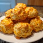 A stack of freshly baked cream cheese sausage balls topped with melted cheddar cheese on a white plate.