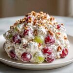 A mound of creamy chicken salad chick grape salad mixed with red and green grapes and topped with chopped pecans.