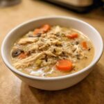 Close-up of a hearty bowl of creamy wild rice soup filled with shredded chicken, bright orange carrots, and mushrooms.