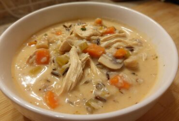 Close-up of a hearty bowl of creamy wild rice soup loaded with shredded chicken, carrots, celery, and mushrooms.