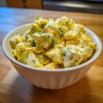A white bowl filled with chunky, creamy egg salad recipe, topped with fresh dill and chopped celery.