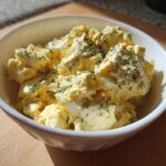 Close-up of a creamy egg salad recipe topped with fresh dill and black pepper in a white bowl.