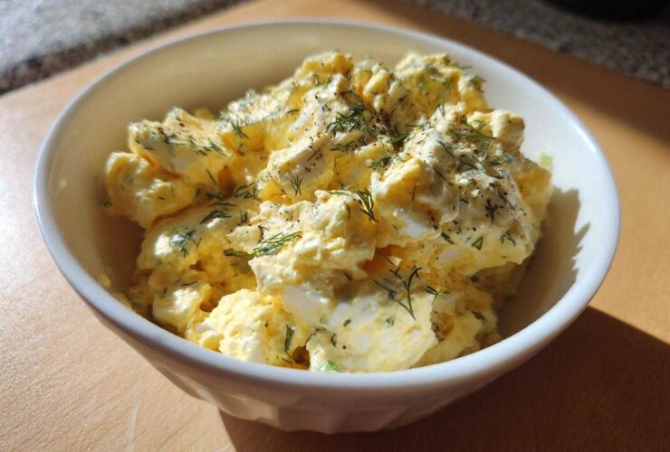 Close-up of a creamy egg salad recipe topped with fresh dill and black pepper in a white bowl.