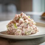 A mound of creamy ham salad mixed with celery and seasonings, served on a white plate.