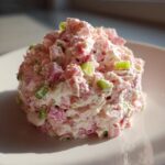 A mound of creamy ham salad mixed with diced pink ham and green celery, served on a white plate.