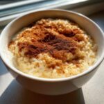 A close-up of a bowl of creamy rice pudding generously dusted with ground cinnamon.