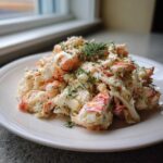 A mound of creamy seafood salad featuring chunks of white and pink shellfish, topped generously with fresh dill.