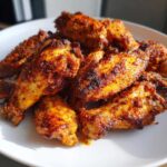 A close-up photo of a pile of perfectly seasoned and crispy air fryer chicken wings on a white plate.
