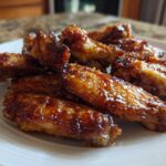 Close-up of several perfectly crispy, glazed chicken wings piled on a white plate.