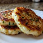 Three perfectly golden brown, crispy mashed potato cakes stacked slightly on a white plate, garnished with chives.