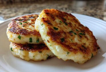 Three perfectly golden brown, crispy mashed potato cakes stacked slightly on a white plate, garnished with chives.