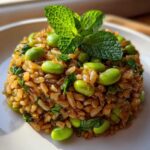 A molded portion of crispy rice salad mixed with bright green edamame and topped with fresh mint leaves.