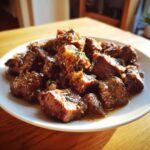 Close-up of tender, saucy crockpot steak cubes garnished with herbs on a white plate.