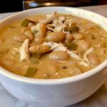 Close-up of a white bowl filled with creamy crockpot white chicken chili, featuring white beans, shredded chicken, and green peppers.