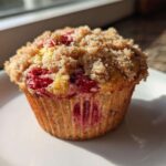 A close-up of a single, freshly baked strawberry muffins topped with a generous layer of brown sugar streusel.