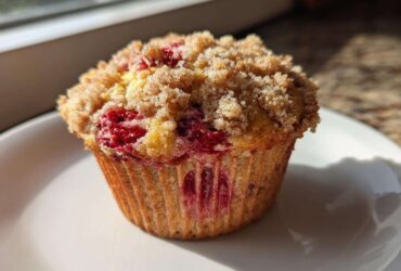 A close-up of a single, freshly baked strawberry muffins topped with a generous layer of brown sugar streusel.