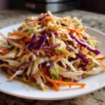 Close-up of a vibrant, crunchy cabbage salad featuring shredded green and purple cabbage and carrots with a light dressing.