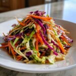 A close-up of a vibrant, crunchy cabbage salad featuring shredded purple cabbage, green cabbage, and carrots tossed in a savory dressing.