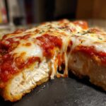 Close-up of Easy Chicken Parmesan cut in half showing juicy white meat, marinara sauce, and melted, stringy mozzarella cheese.