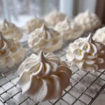 Close-up of freshly piped, white meringue cookies cooling on a wire rack.