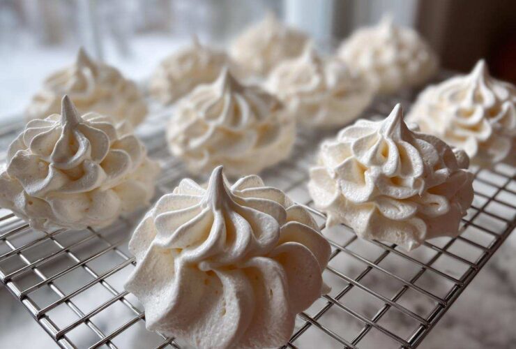 Close-up of freshly piped, white meringue cookies cooling on a wire rack.