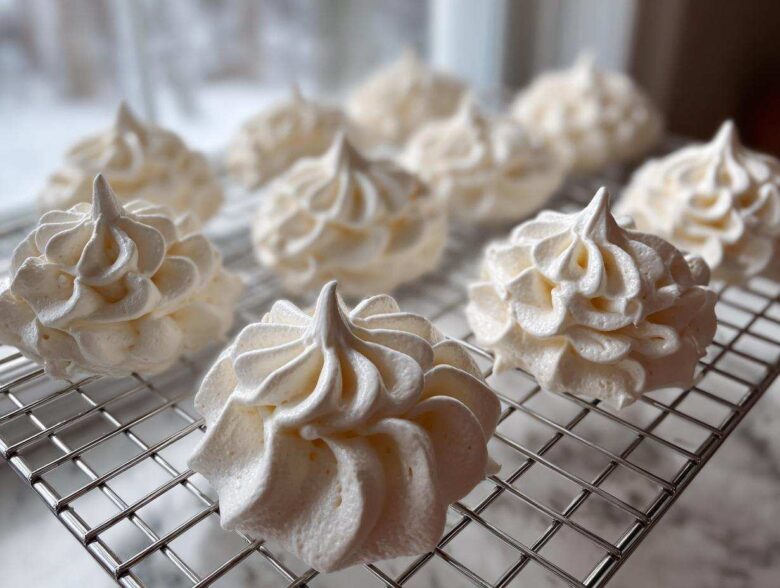 Close-up of freshly piped, white meringue cookies cooling on a wire rack.