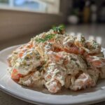 A generous serving of creamy seafood salad with visible shrimp pieces, garnished with fresh dill, on a white plate.