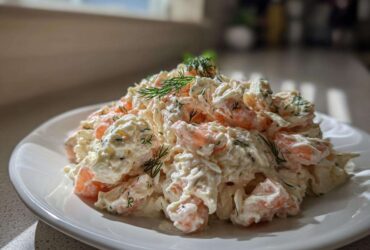 A generous serving of creamy seafood salad with visible shrimp pieces, garnished with fresh dill, on a white plate.
