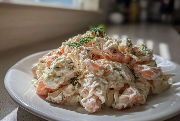 A generous serving of creamy seafood salad with visible shrimp pieces, garnished with fresh dill, on a white plate.