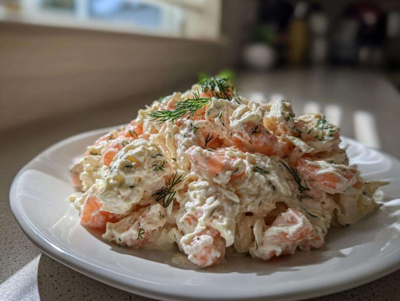 A generous serving of creamy seafood salad with visible shrimp pieces, garnished with fresh dill, on a white plate.