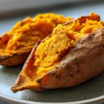 Close-up of a fluffy baked sweet potato cut in half, showing the bright orange interior.