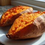 Two halves of perfectly cooked baked sweet potatoes showing bright orange, fluffy insides on a white plate.