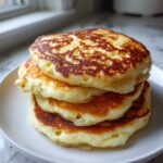 A stack of three fluffy greek yogurt pancakes with golden brown edges on a white plate.