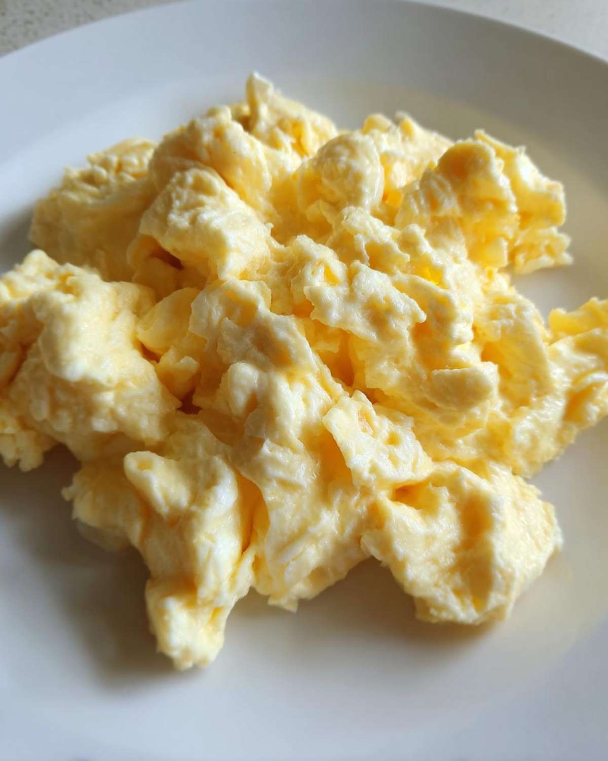 Close-up of perfectly cooked, fluffy scrambled eggs piled on a white plate.