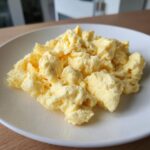 Close-up of perfectly cooked, fluffy scrambled eggs served on a white plate.