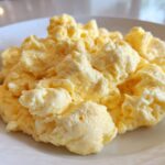 Close-up of perfectly cooked, fluffy scrambled eggs piled high on a white plate.