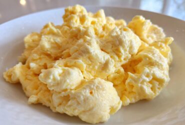 Close-up of perfectly cooked, fluffy scrambled eggs piled high on a white plate.