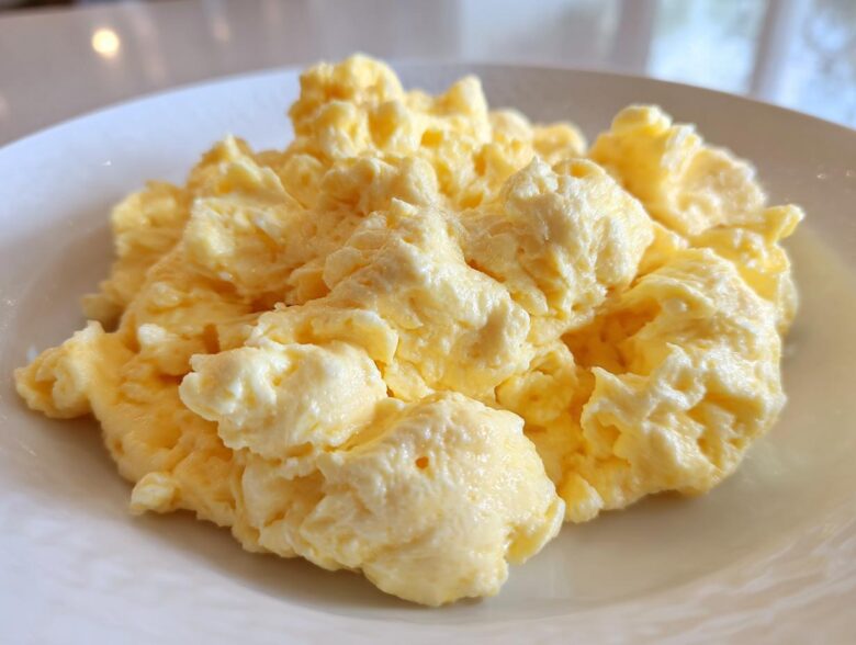 Close-up of perfectly cooked, fluffy scrambled eggs piled high on a white plate.