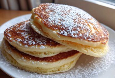 A close-up stack of three thick, fluffy sourdough pancakes dusted generously with powdered sugar.