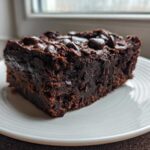 A close-up of a dense, fudgy slice of sweet potato brownies topped with chocolate chips on a white plate.