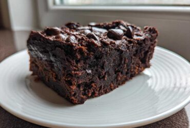 A close-up of a dense, fudgy slice of sweet potato brownies topped with chocolate chips on a white plate.