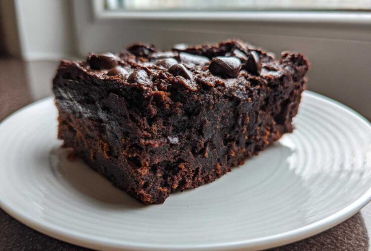 A close-up of a dense, fudgy slice of sweet potato brownies topped with chocolate chips on a white plate.