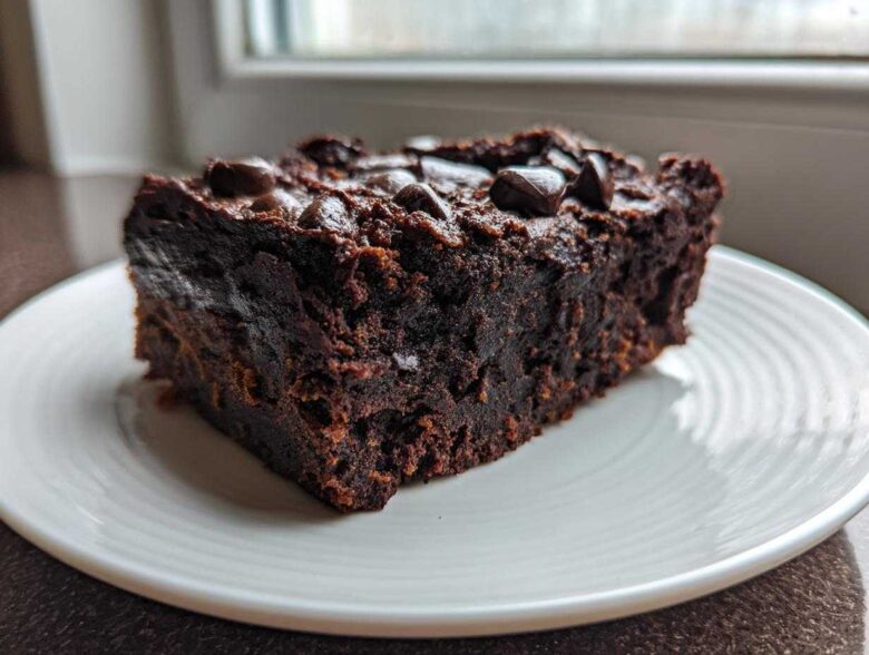 A close-up of a dense, fudgy slice of sweet potato brownies topped with chocolate chips on a white plate.